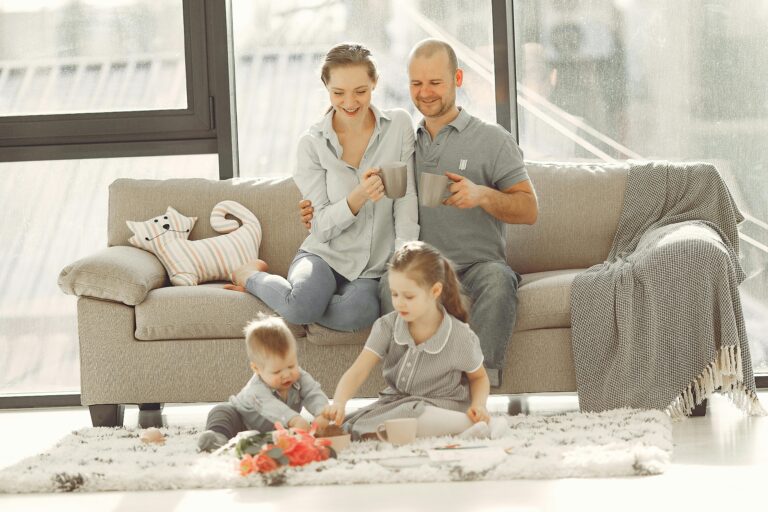 Cheerful family wearing casual clothes sitting in living room while playing and drinking tea during weekend at home in morning